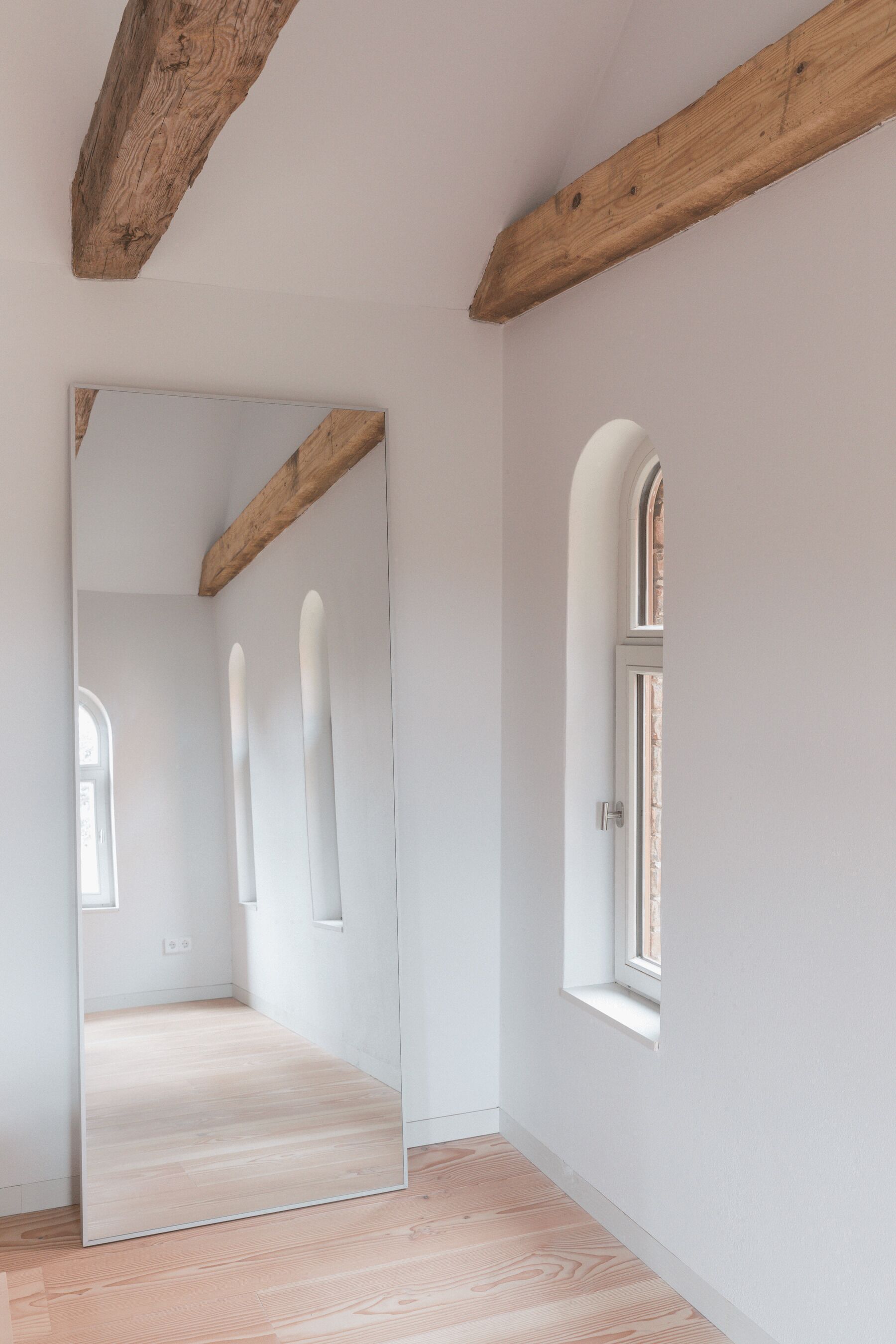 Une pièce dotée d’un grand miroir, de poutres en bois, d’une fenêtre et d’un plancher de couleur claire.