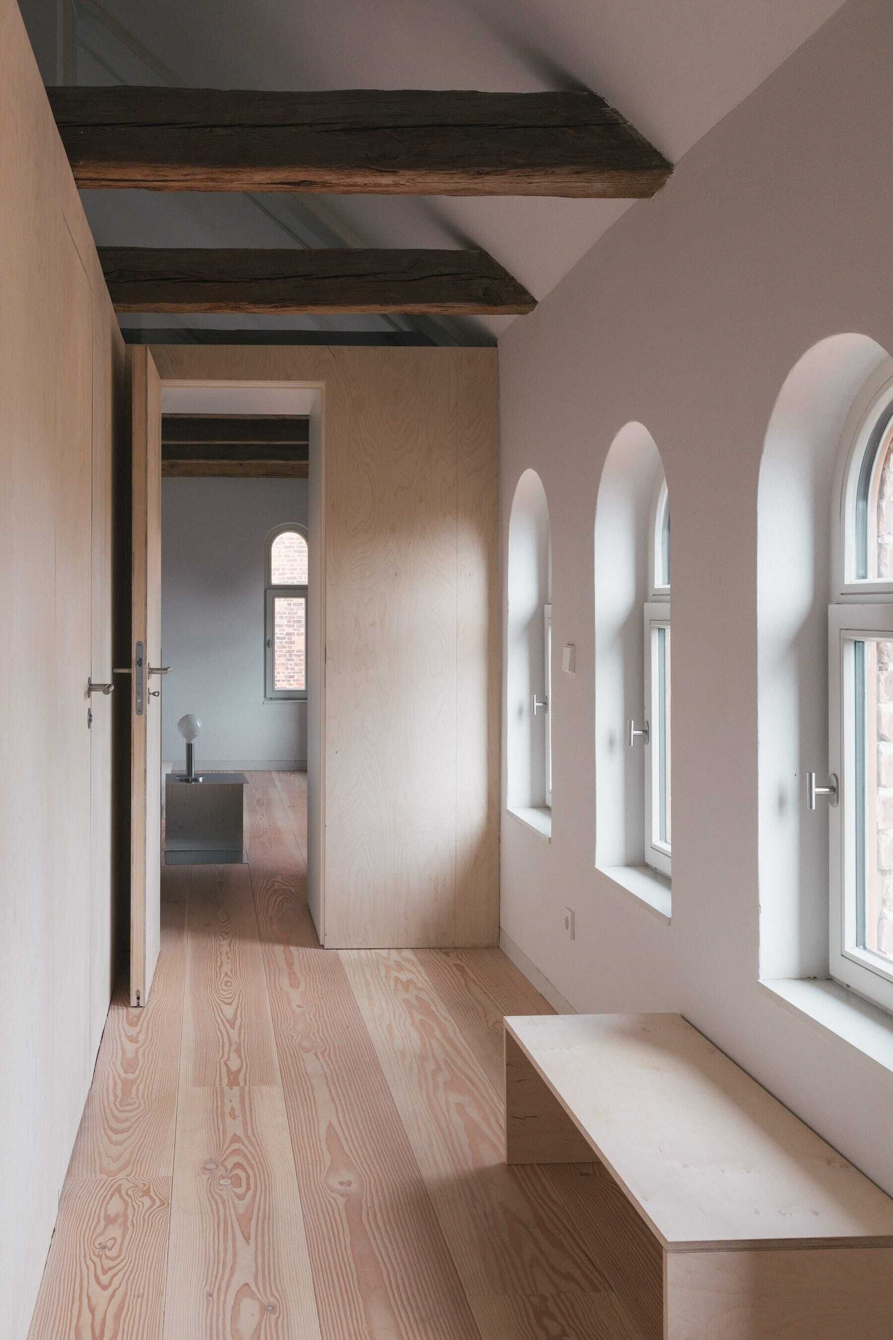 Ein modernes Interieur mit Holzböden, einer Bank und Bogenfenstern.