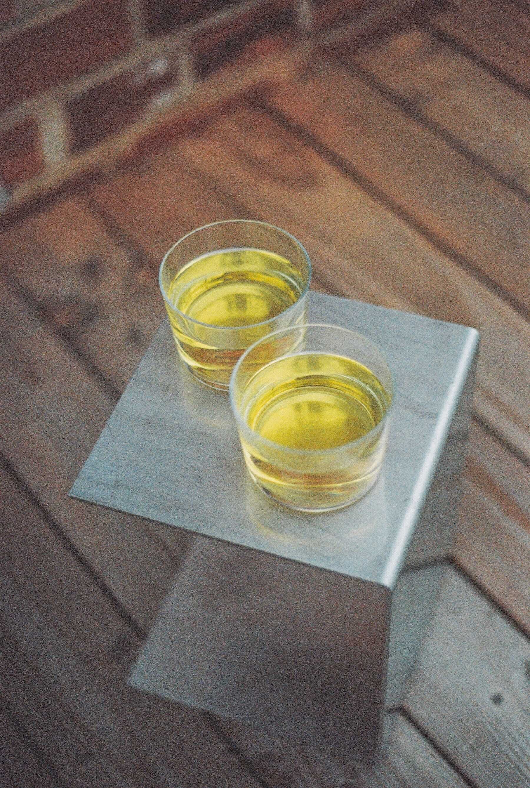 Two glasses of yellow liquid on a metal tray on a wooden floor.
