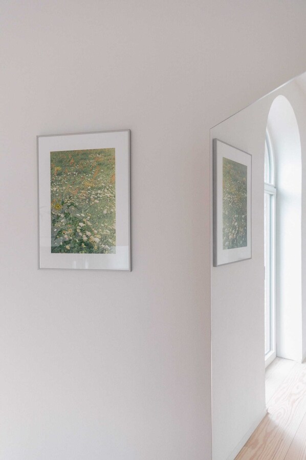 A hallway with two framed artworks on the walls and a window on the right.