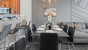 Uma área de refeições moderna com mesa de vidro, cadeiras pretas e um lustre.