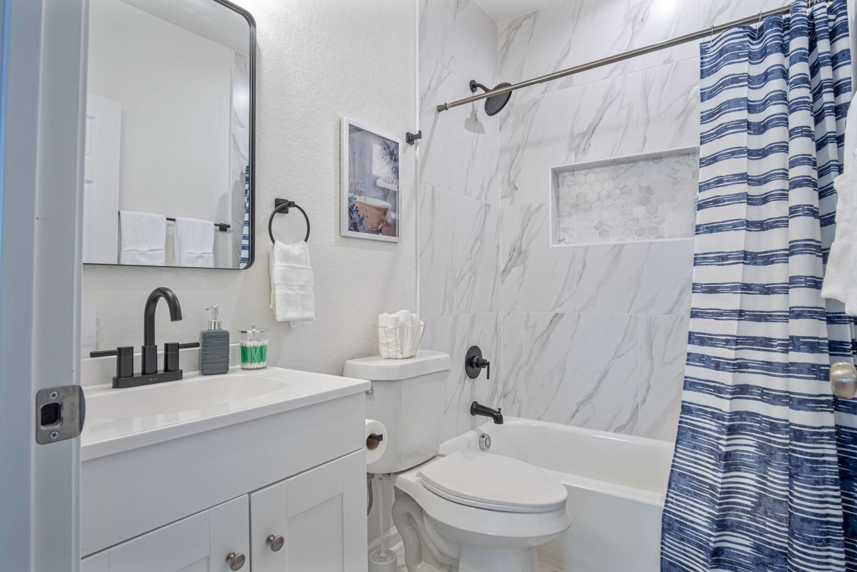 A bathroom with a white sink, toilet, and bathtub, marble walls, and a shower curtain.
