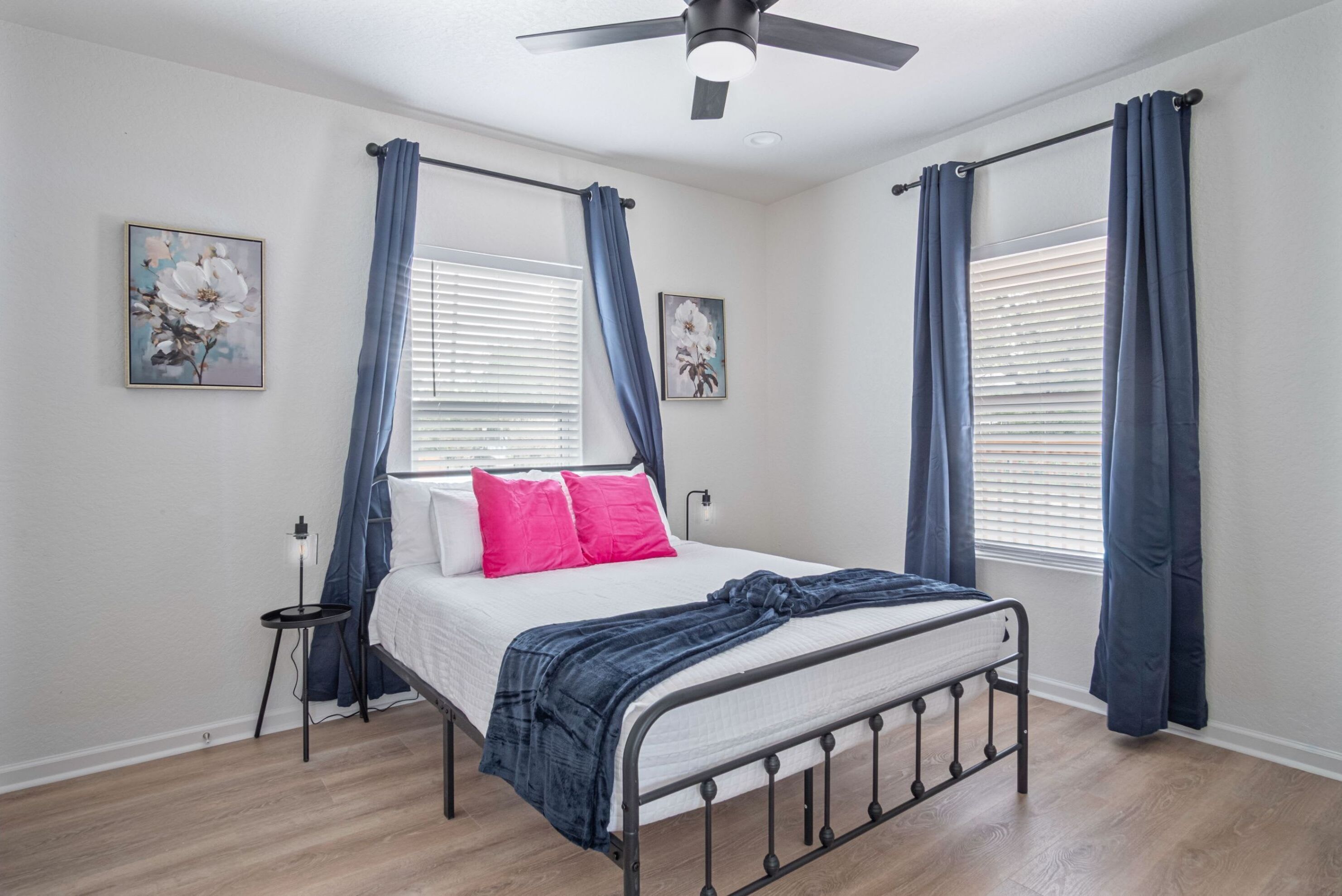 A bedroom with a bed, a ceiling fan, and two windows with curtains.