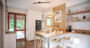 A modern kitchen with a wooden island, bar stools, a microwave, and a hanging light fixture.