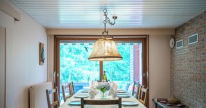 Spiseområde med et bord dækket til fire personer, en hængende lampe og udsigt gennem et vindue.