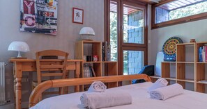Un dormitorio con cama, dos lámparas de noche, una silla de madera, un escritorio, una estantería y un dardo.