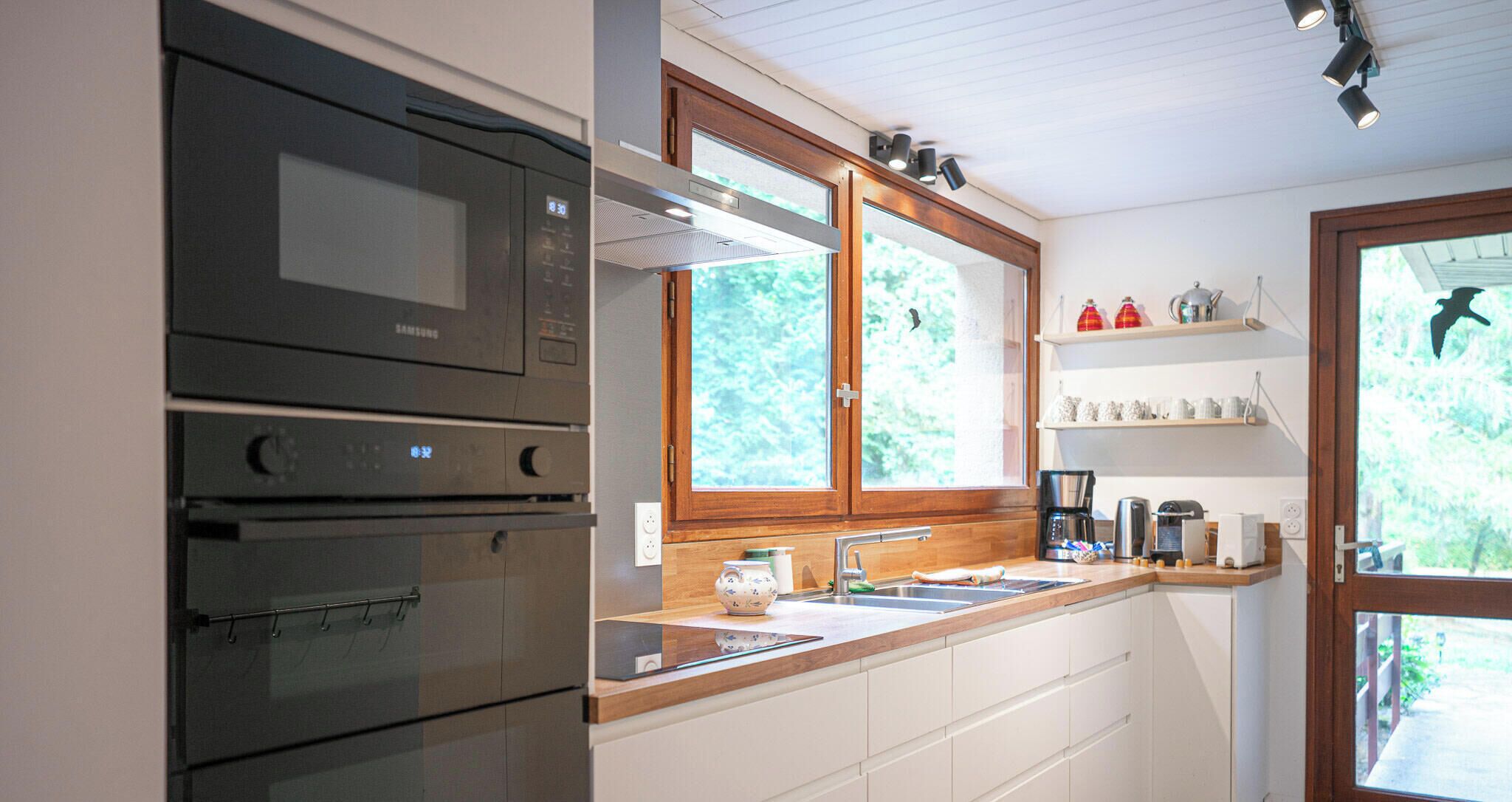A kitchen with a microwave, oven, and a window above the sink.