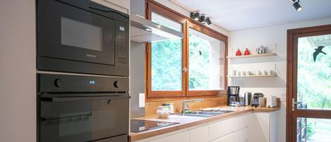 A kitchen with a microwave, oven, and a window above the sink.