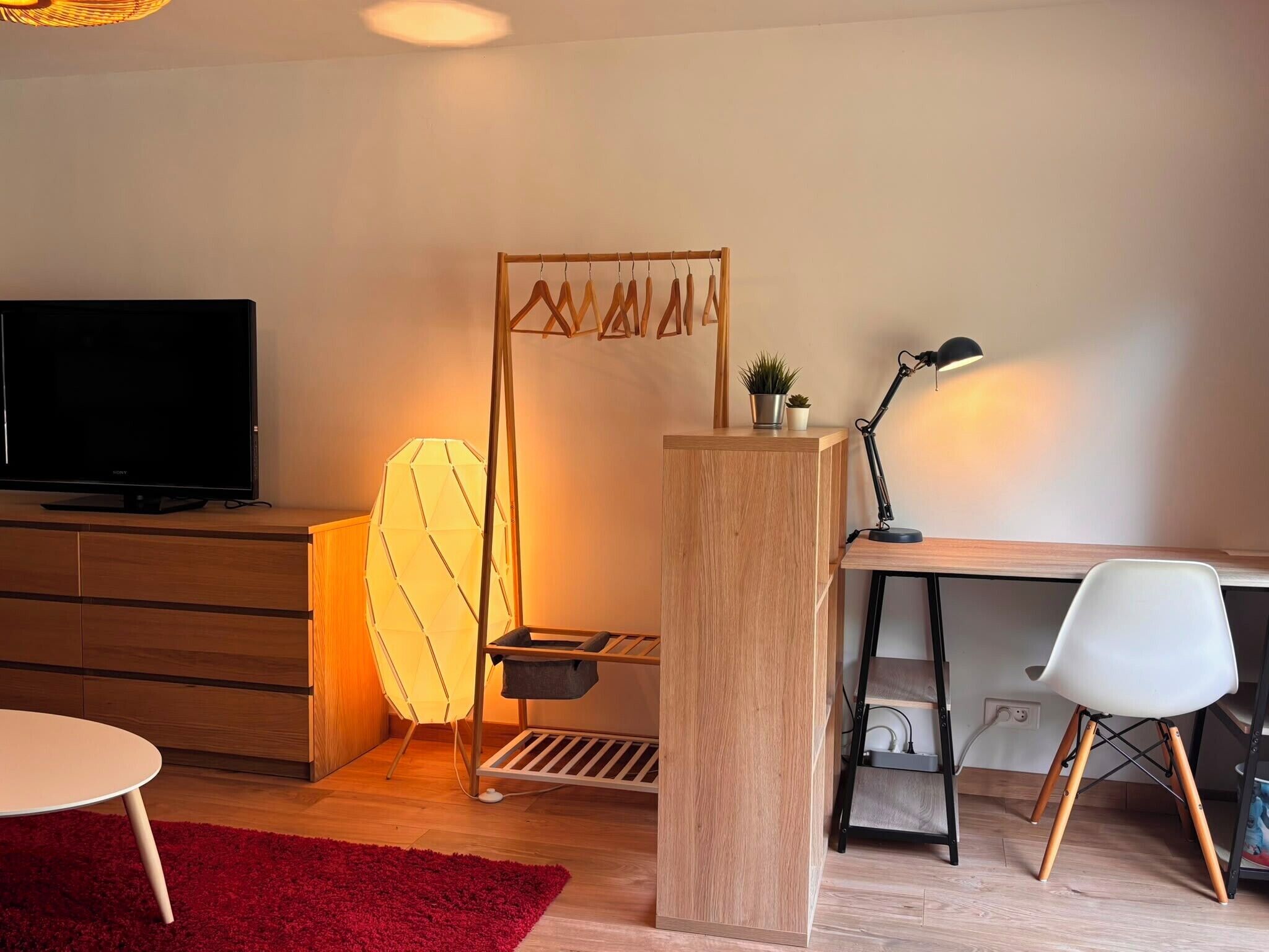 A modern room with a TV, desk, chair, lamp, and a red rug.