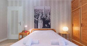Une chambre d’hôtel avec un lit, une table de chevet avec une lampe, une armoire en bois et un tableau représentant un paysage urbain accroché au mur.