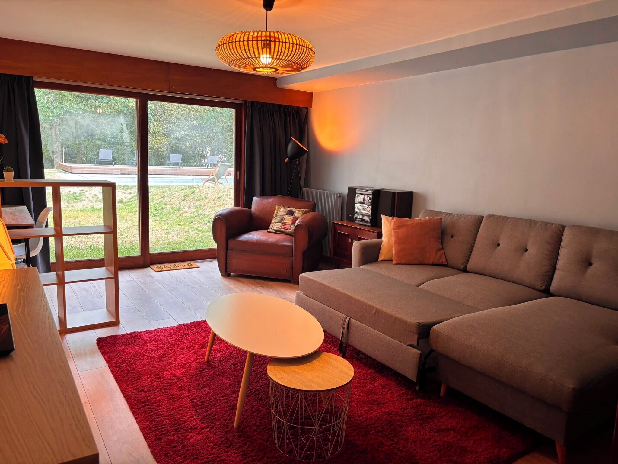 A modern living room with a sofa, a coffee table, a TV, and a large window offering a view of the outdoors.