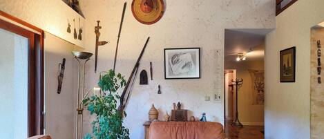 Una habitación con diseño tradicional, que presenta un suelo de madera, una planta y diversos objetos culturales en las paredes.