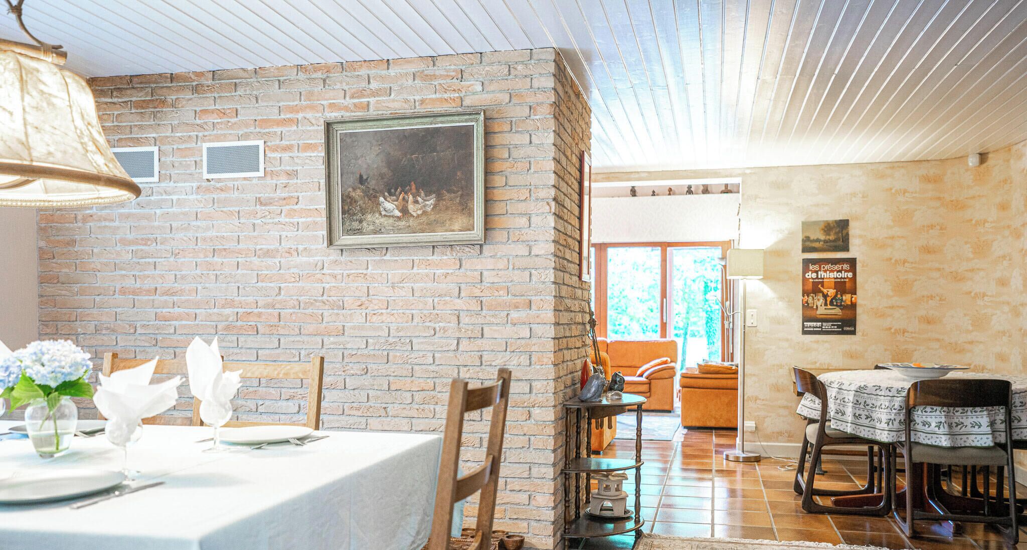 Een eetgedeelte met een bakstenen muur, een lijstwerk schilderij en een tafel gedekt voor twee personen.