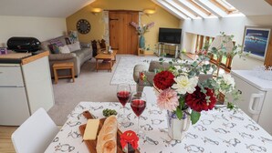 A cozy living room with a dining area, featuring a table set with bread, wine glasses, and flowers. - The Dairy (Axminster)