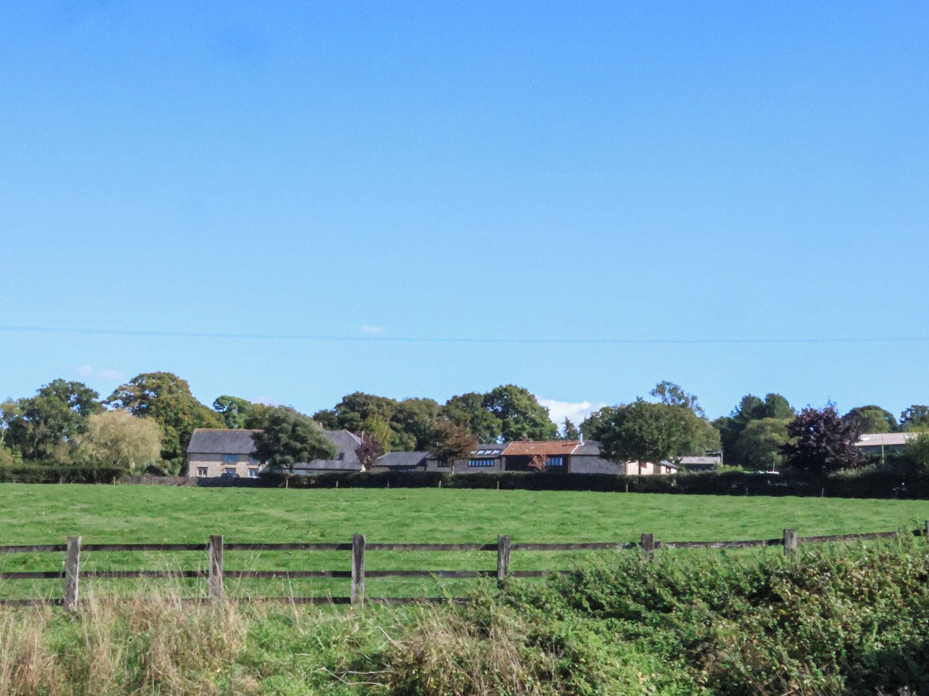 Un paysage rural avec une clôture en bois, des champs verdoyants et des maisons aux toits rouges.