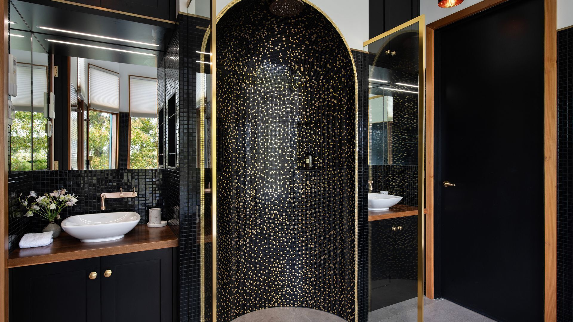 Un baño moderno con paredes de azulejos negros, un lavamanos blanco y un espejo grande.