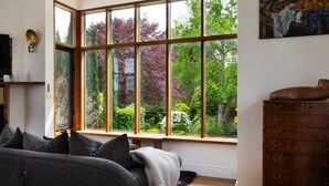 Ein Zimmer mit einem großen Erkerfenster, einem Holzschrank und einem grauen Sofa.