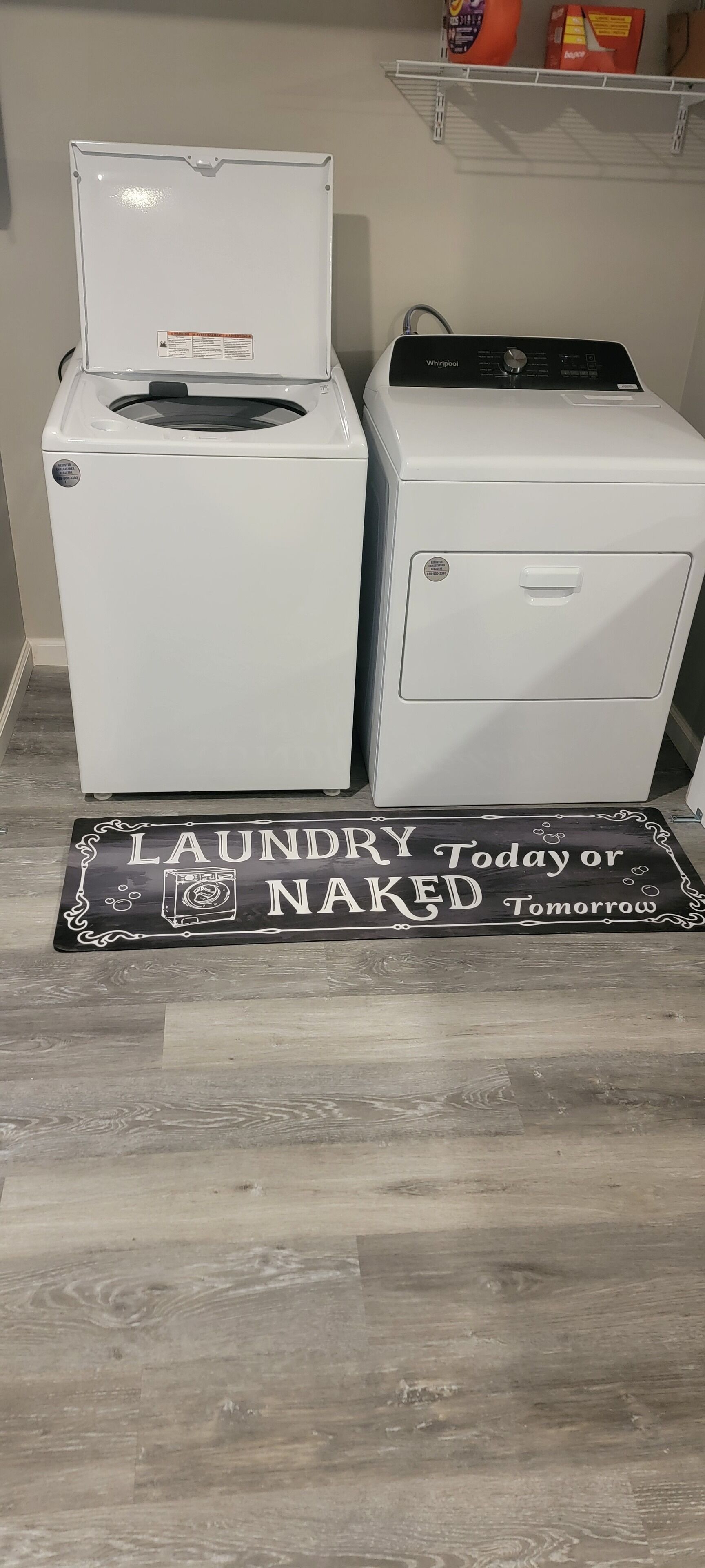 A laundry area with two white washing machines and a black doormat with white text.