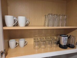 Et skab med hylder, der indeholder hvide krus, glas og en kaffemaskine.