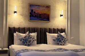A hotel room with a bed, two pillows, a headboard, and a painting on the wall. - Isakhoja Hotel (Khiva)