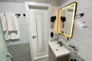 Ein Badezimmer mit weißer Tür, einem Spiegel mit LED-Beleuchtung, einem Föhn und einem Waschbecken.