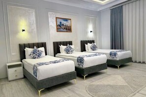 Ein Hotelzimmer mit drei Betten, einem Nachttisch, einem Gemälde und einem großen Fenster mit Vorhängen.