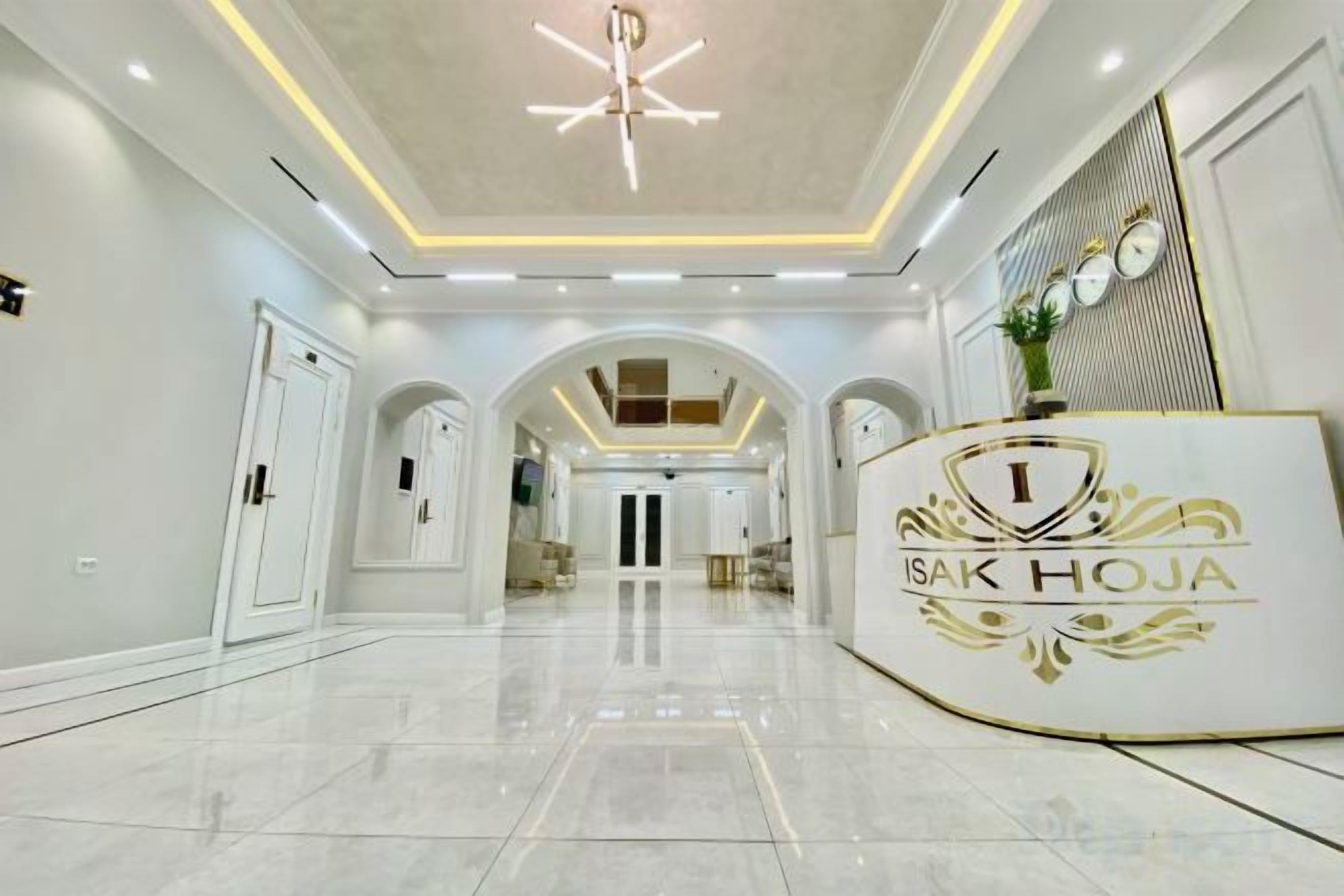 Un'area reception di un hotel con un pavimento in marmo lucido, una scrivania della reception con un logo e un soffitto alto con illuminazione a incasso.