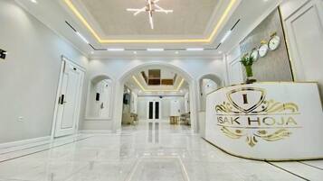 Un'area reception di un hotel con un pavimento in marmo lucido, una scrivania della reception con un logo e un soffitto alto con illuminazione a incasso.