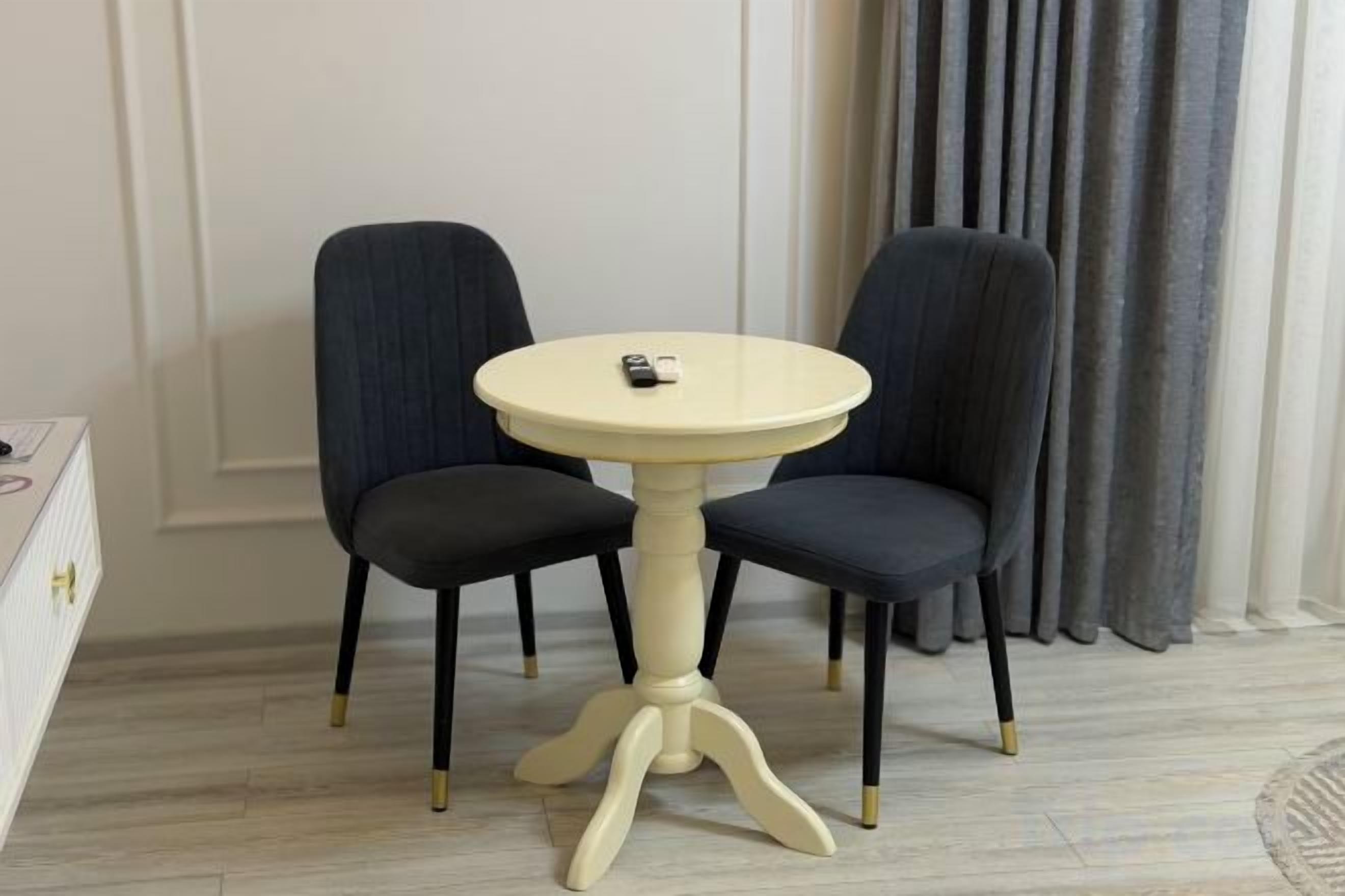 A round table with two chairs, a remote control on the table, and a curtain in the background.