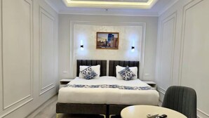 A hotel room with a bed, bedside tables, a chair, a round table, and a wall-mounted picture. - Isakhoja Hotel (Khiva)
