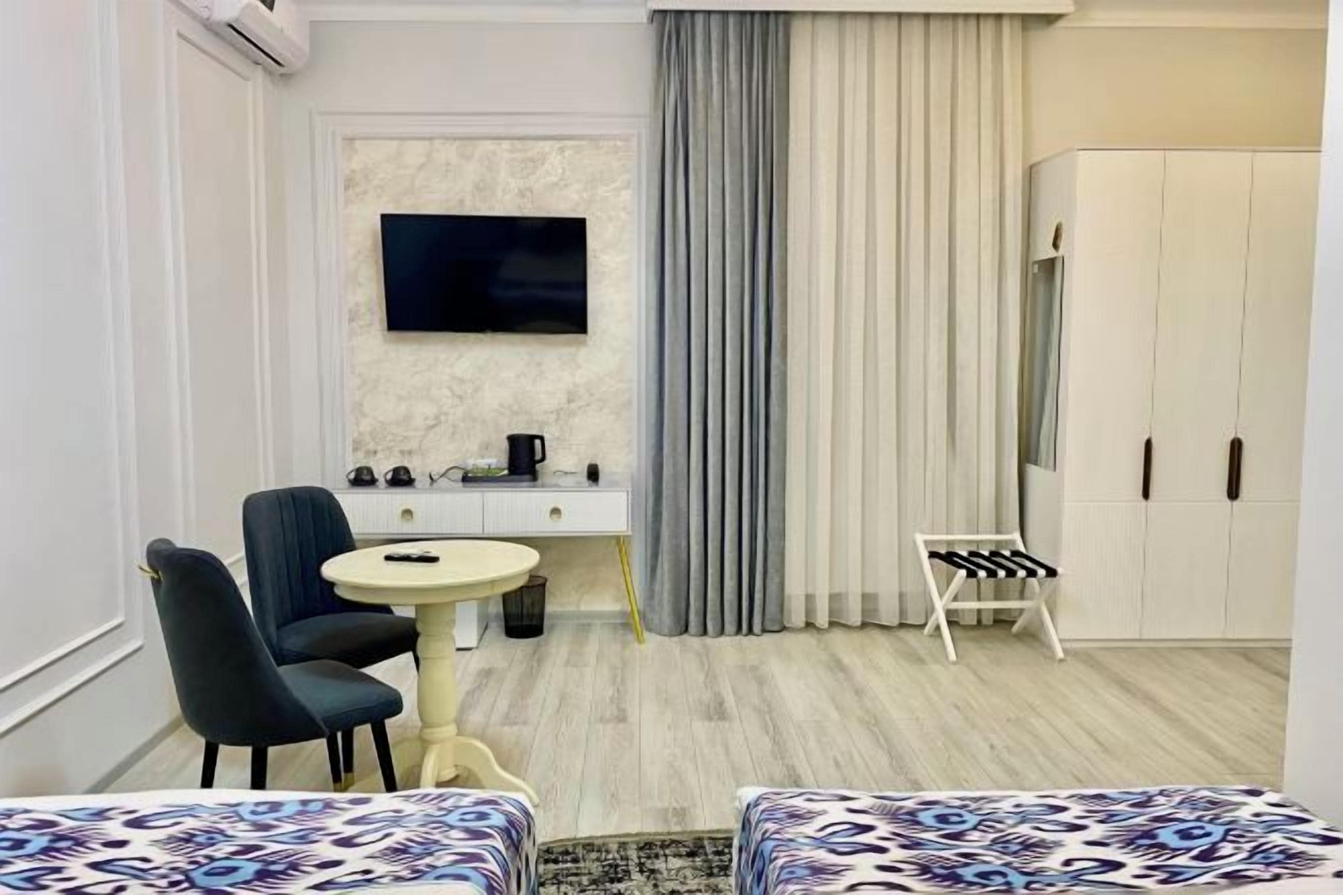 A hotel room with a bed, a desk with a chair, a television, a wardrobe, and a small table with a chair.