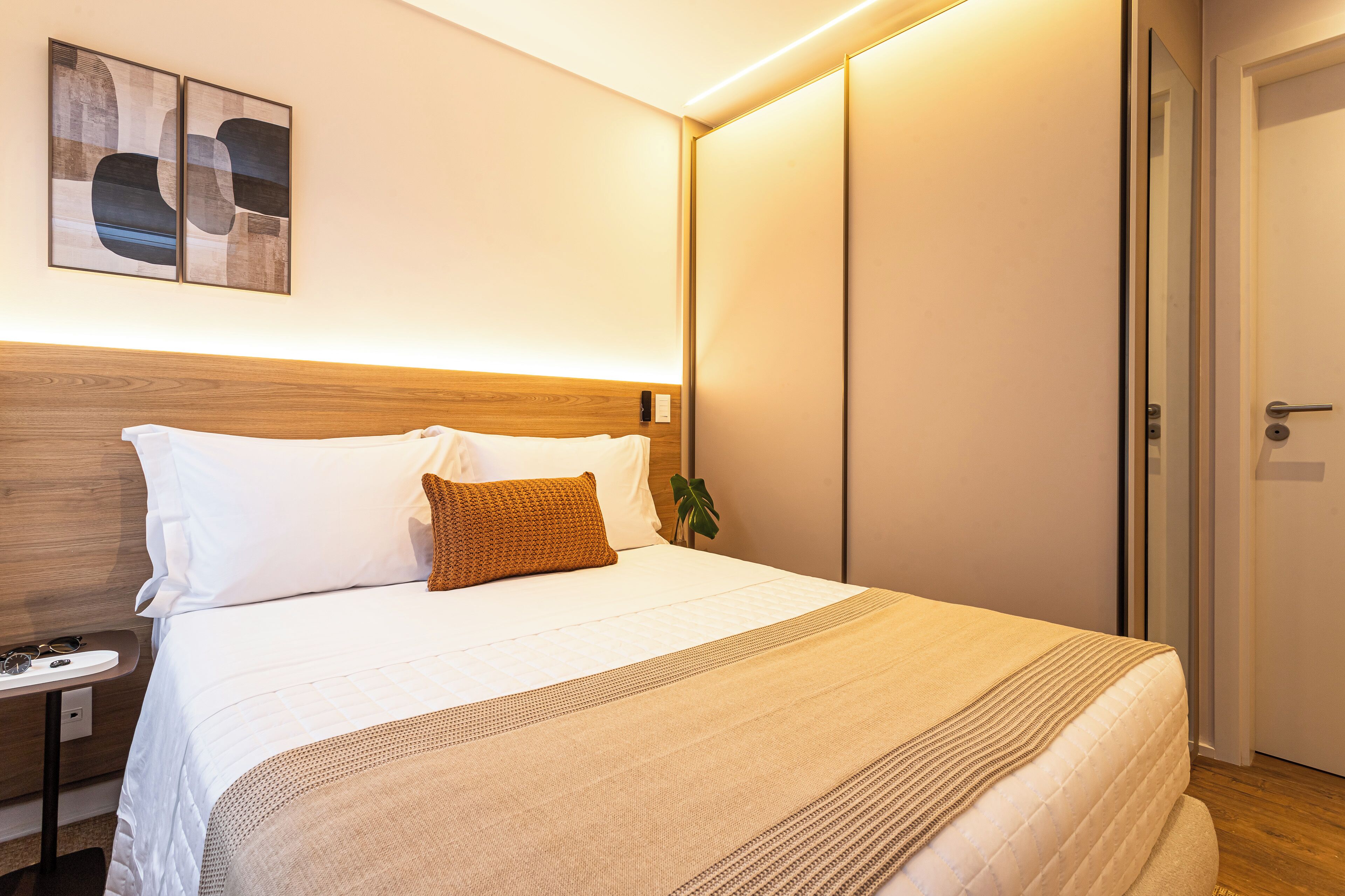 A neatly made bed with white and brown bedding, a bedside table with glasses, and a wall-mounted abstract art piece.