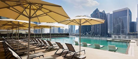 A rooftop pool area with sun loungers and umbrellas, overlooking a city skyline.