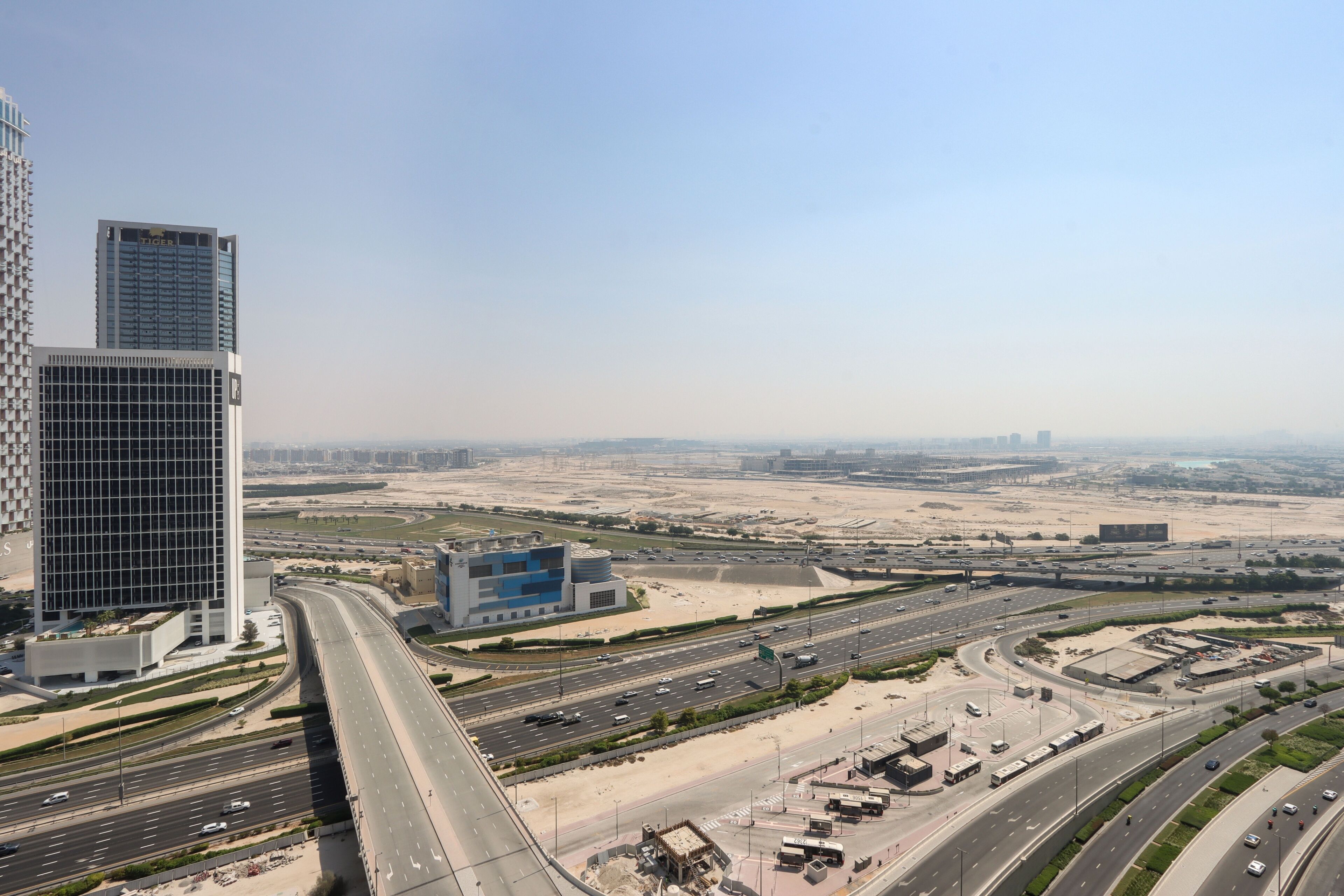 A high-rise building with a modern design, surrounded by a well-maintained urban area with multiple roads and clear skies.