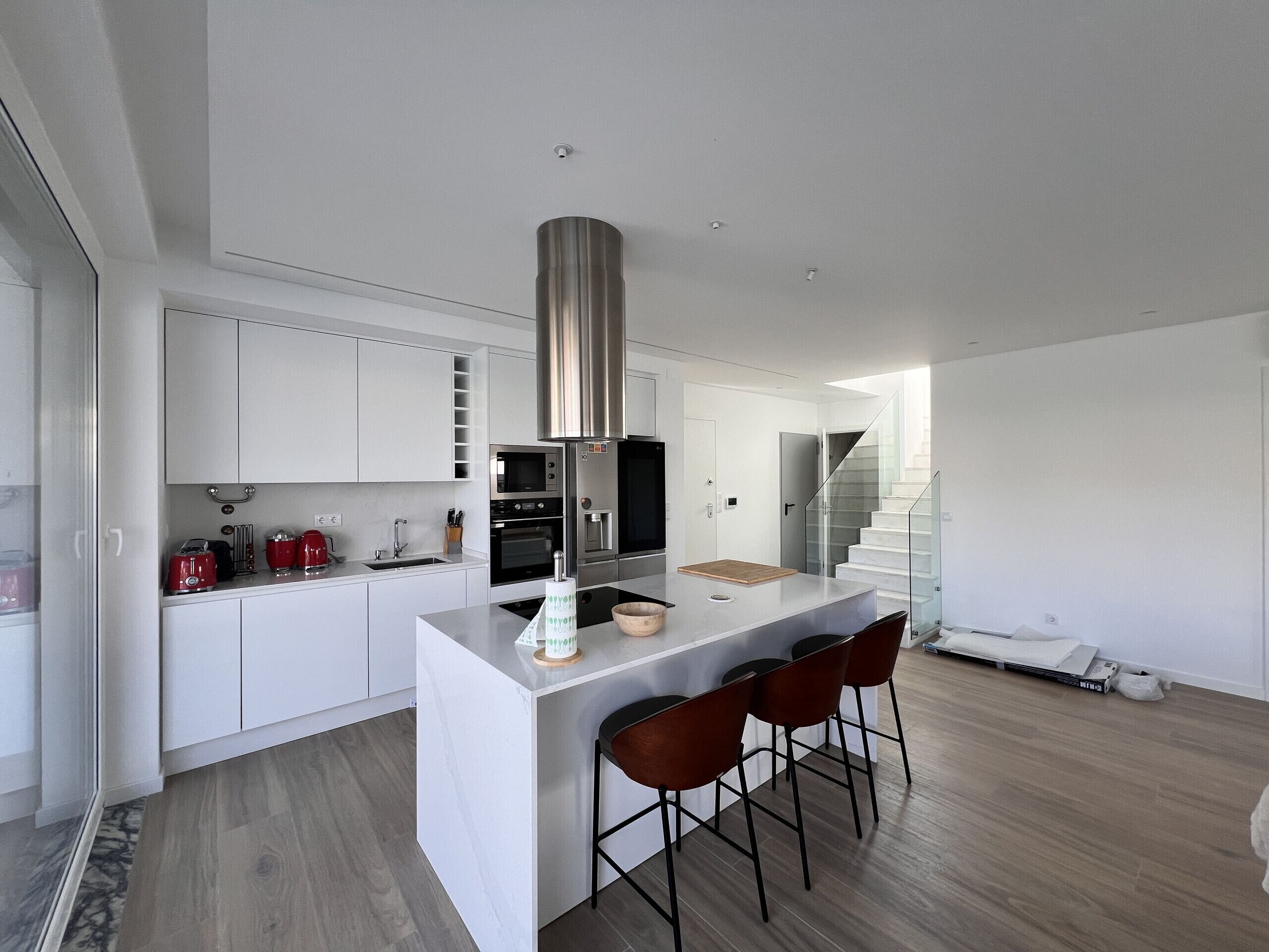 A modern kitchen with white cabinetry, stainless steel appliances, and a central island with bar stools.