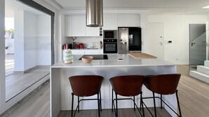 A modern kitchen with a central island, stainless steel appliances, and a minimalist design. - Villa Das Hortensias (Aroeira)