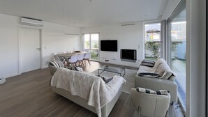 A modern living room with a sofa, a dining table with chairs, a TV, and a fireplace. - Villa Das Hortensias (Aroeira)