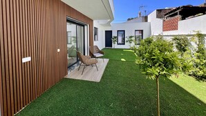 A modern house with a wooden exterior, a small lawn, and two wicker chairs. - Villa Das Hortensias (Aroeira)