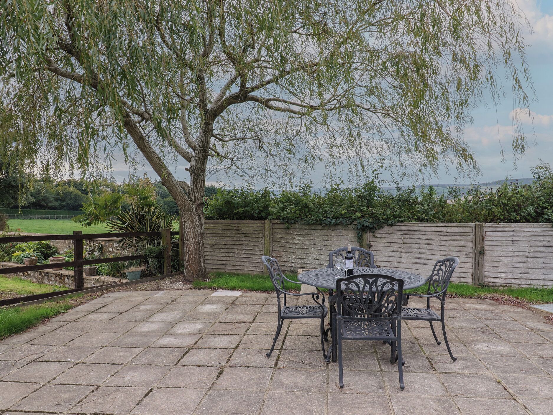 A patio with a table and chairs, a bottle of wine, and a view of a tree and landscape.