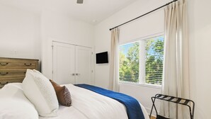 Een slaapkamer met een bed, een houten dressoir, een televisie, een raam met gordijnen en een radiator.