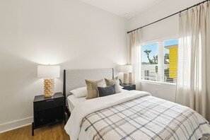 Un dormitori amb un llit, dues taules de nit, una làmpada i una finestra amb cortines.
