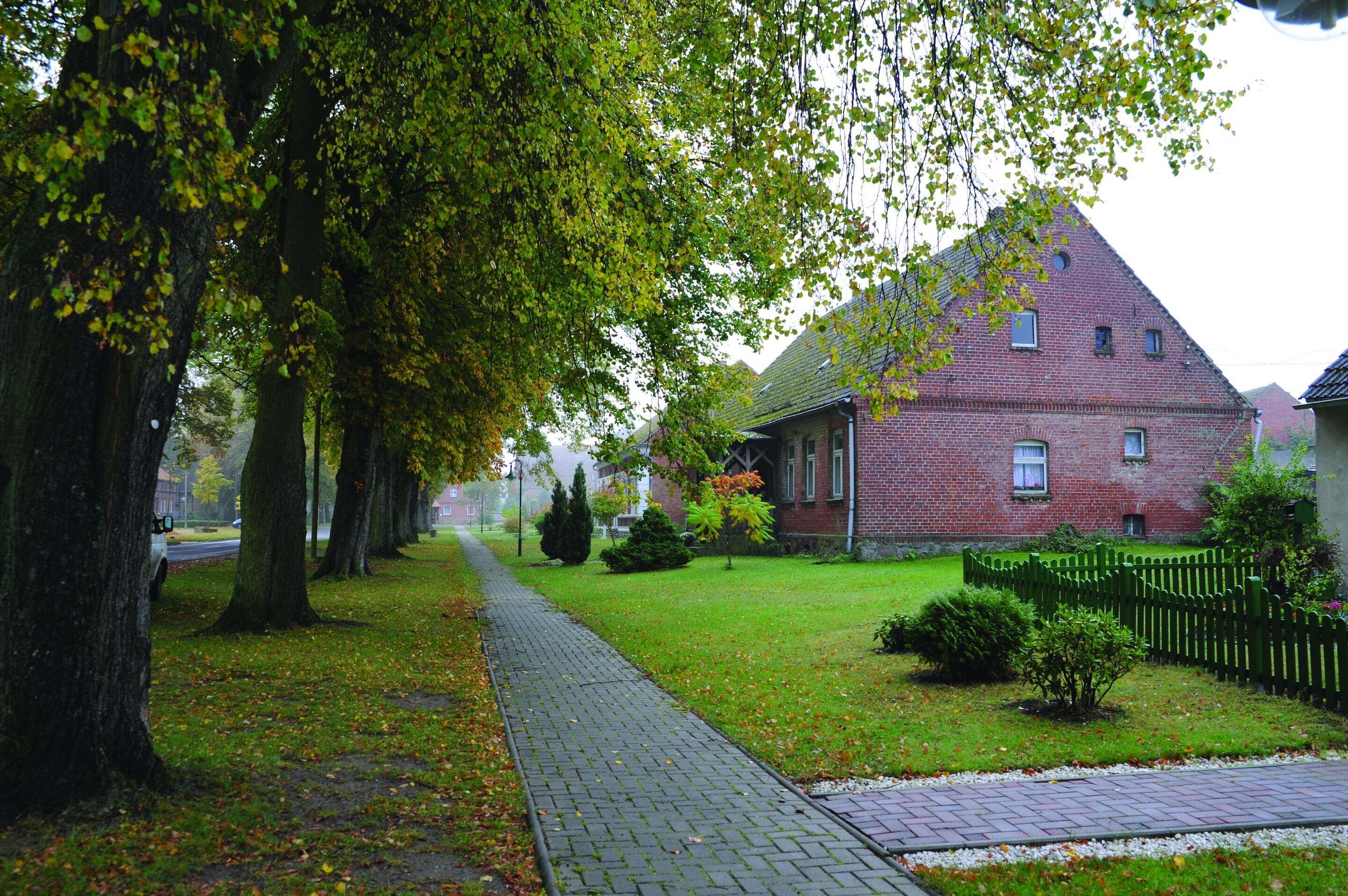 A brick building with a sloped roof, surrounded by a green fence and trees.