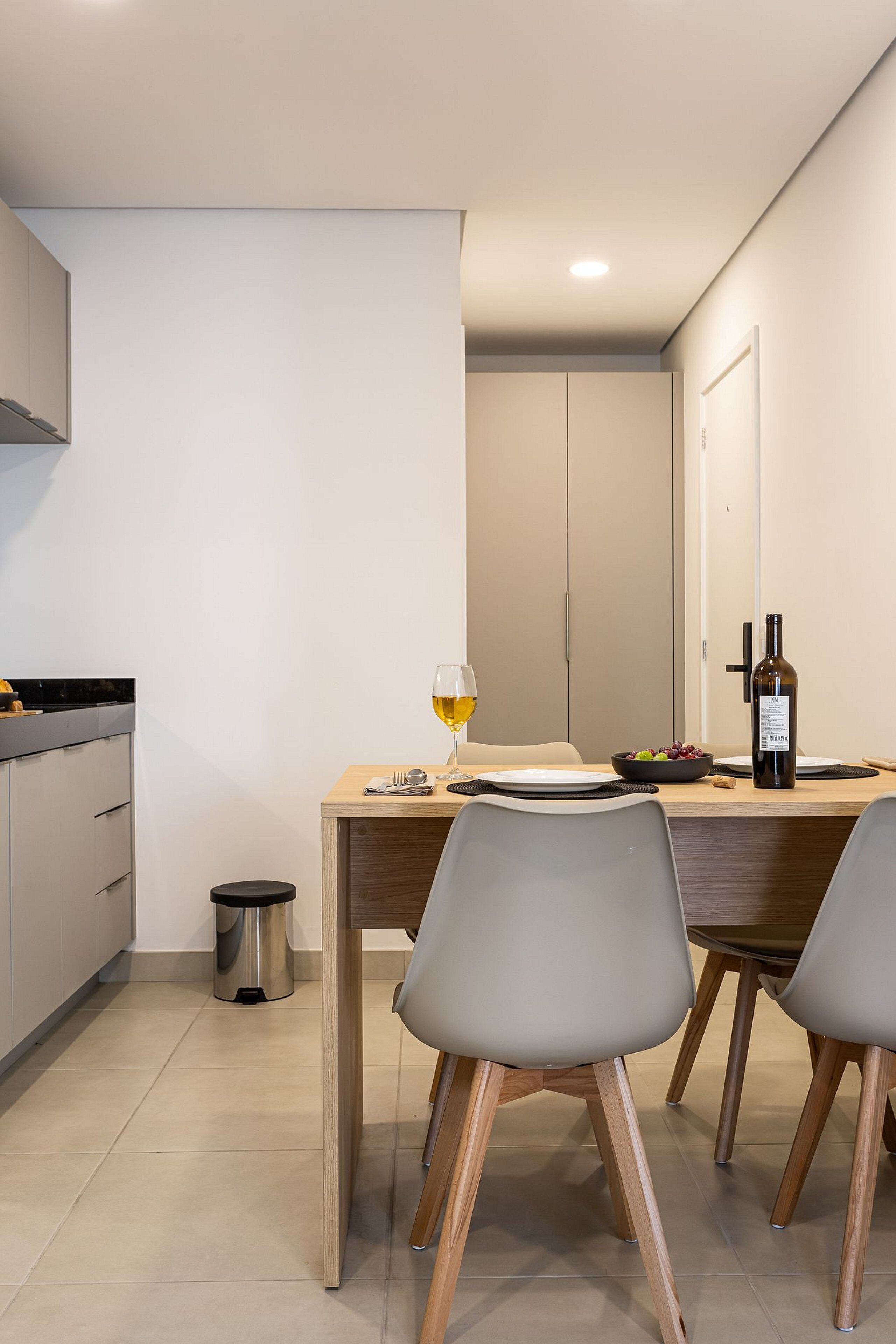 A modern kitchen with a dining table set for two, a wine bottle, and a glass of wine.