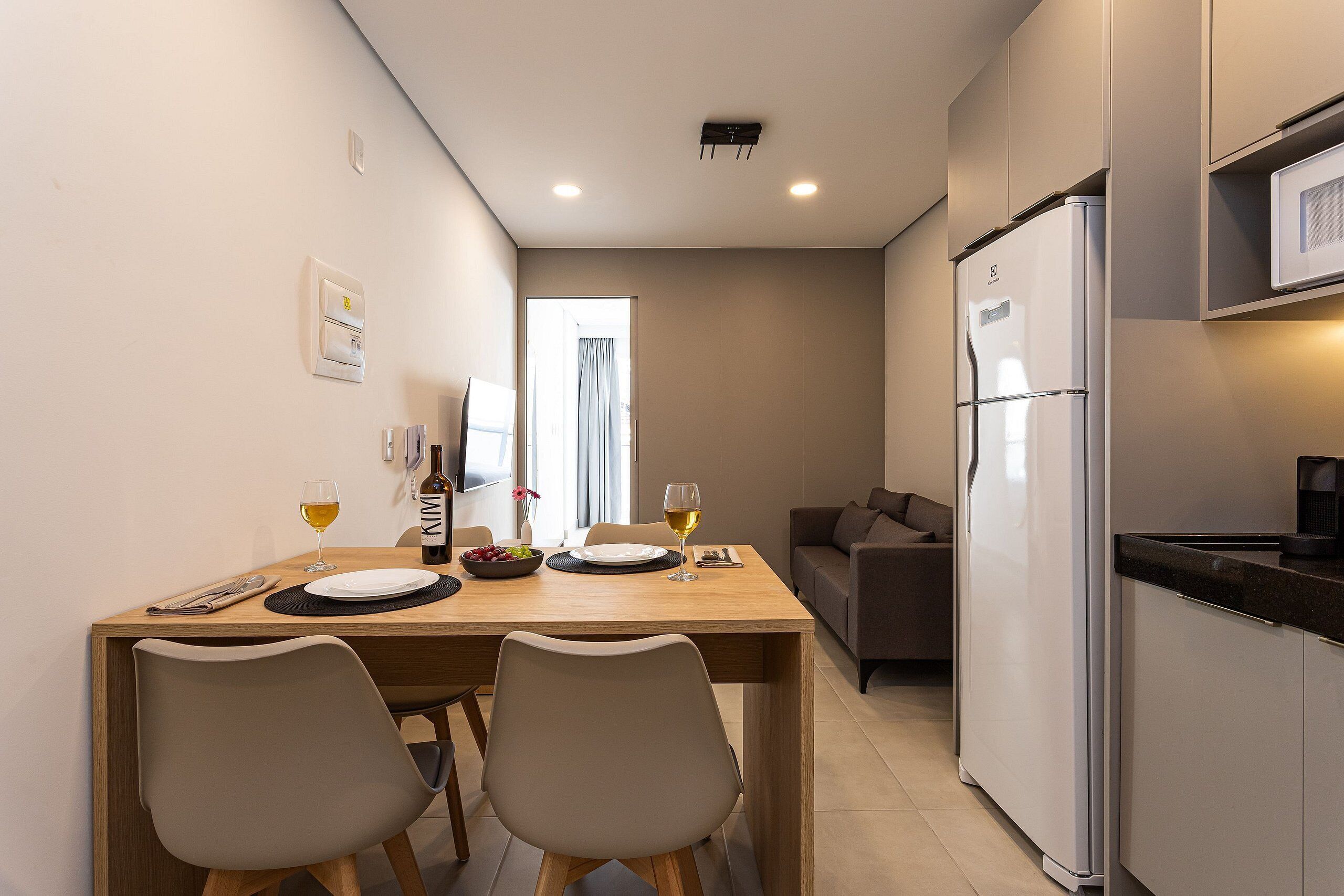 A modern kitchen with a refrigerator, microwave, and dining area with two chairs and a table set for two.