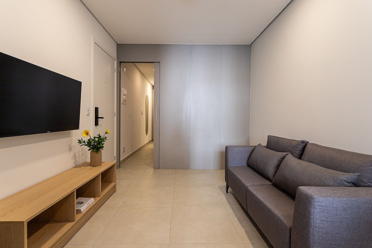 Una sala de estar moderna con un televisor de pantalla plana, un sofá gris y un mueble bajo de madera con un florero.