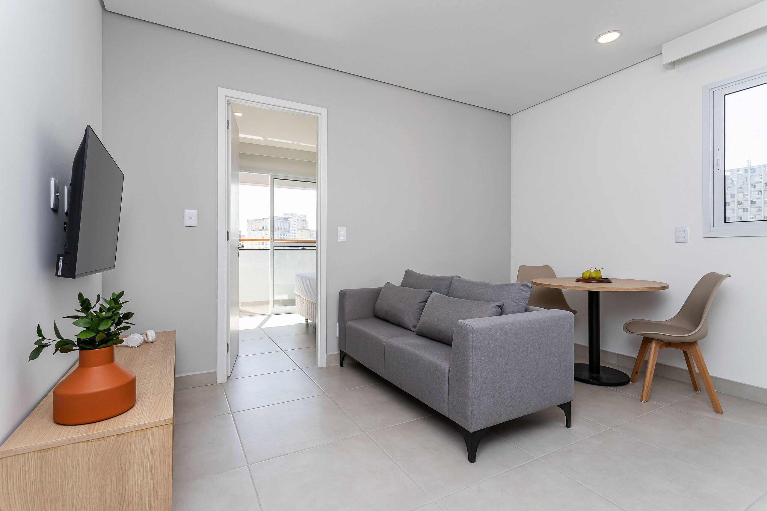 A modern living room with a grey sofa, a small round table, and a TV mounted on the wall.