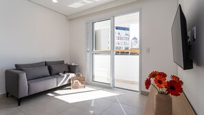 Una sala moderna con un sofá gris, una mesita de madera con un jarrón de flores y un ventanal corredizo que da a un espacio exterior.