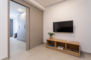 A modern hotel room with a sliding door leading to a hallway, a flat-screen TV mounted on the wall, a wooden console table with a vase and books, and a suitcase in the background. - Aurora - Pr édio novíssimo e completo no coração do Centro, com piscina e academia ao lado do metrô República (São Paulo)