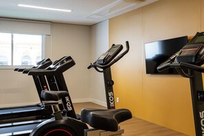 Una palestra con tapis roulant, cyclette e una televisione appesa al muro.