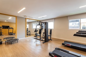 Un gimnasio con cintas de correr, máquinas de pesas y un espejo.